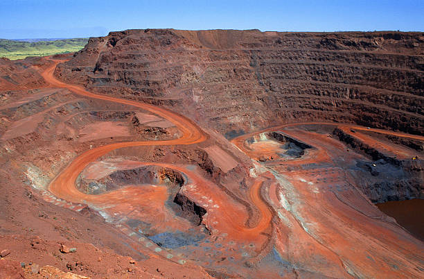 "Looking down on a large open cut iron ore mine in Australiaaas remote Pilbara region.  At the bottom of the pit at the end of the red winding road, a dump truck is being loaded with ore.  Other mine vehicles appear tiny in the huge pit.  Beyond the open cut are green hills.  Taken with permission during a guided tour of the mine."